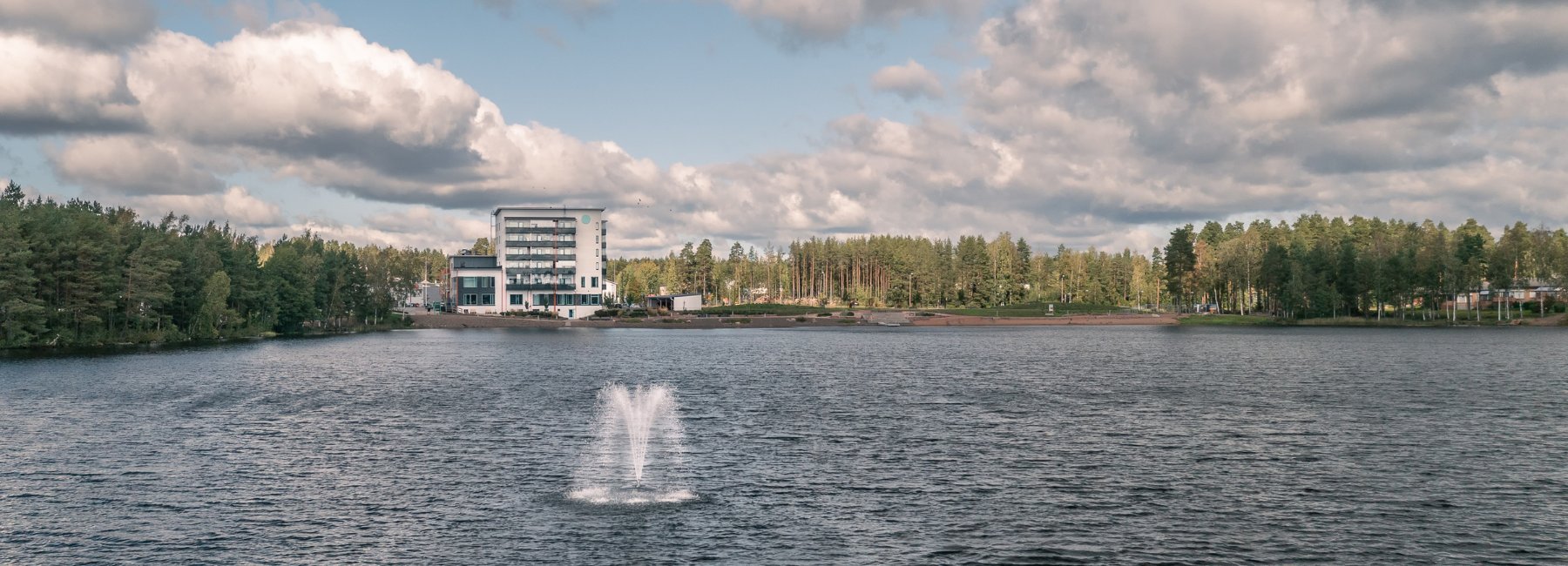 Järvi, jossa suihkulähde ja vastarannalla kerrostalo